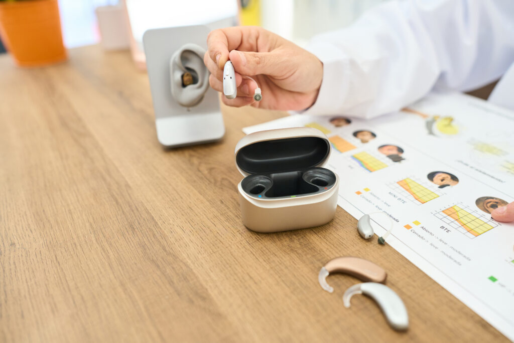 Audiologist holding modern hearing aid at clinic desk